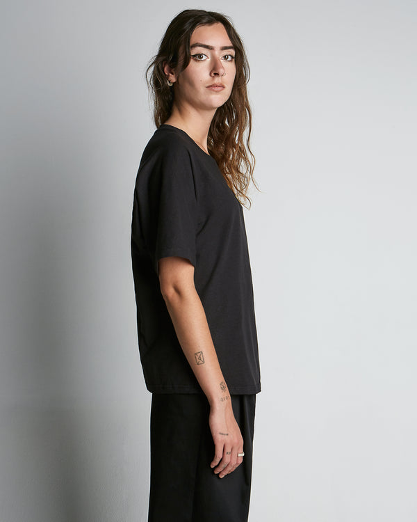 Black, short sleeved t-shirt made of hemp with a yelloe, embroidery logo on the left side of chest. Side view