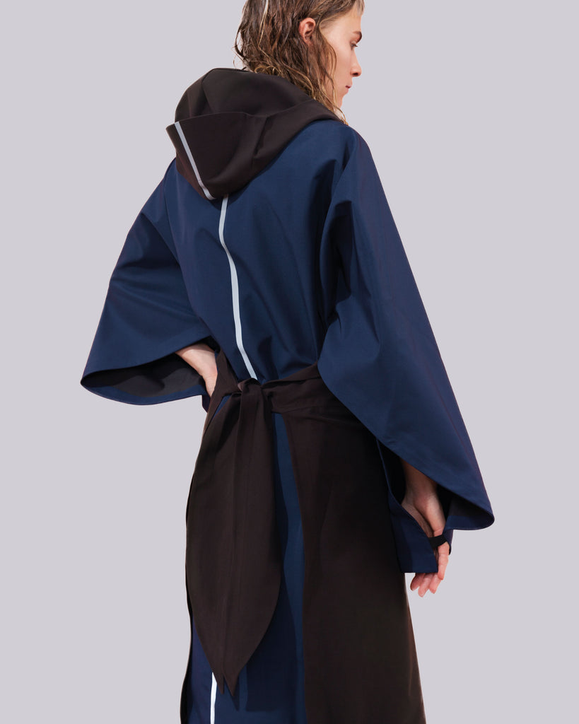 this open cape is a combination of black and blue with a hood and a reflective stripe down the back.