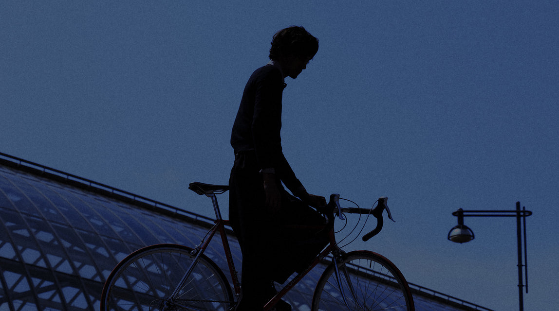 Silhouette of a person wearing the Moxie rainskirt with a bicycle against a dark blue sky