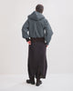 Person wearing a denim hooded jacket and dark rainpants/rainskirt on a white background