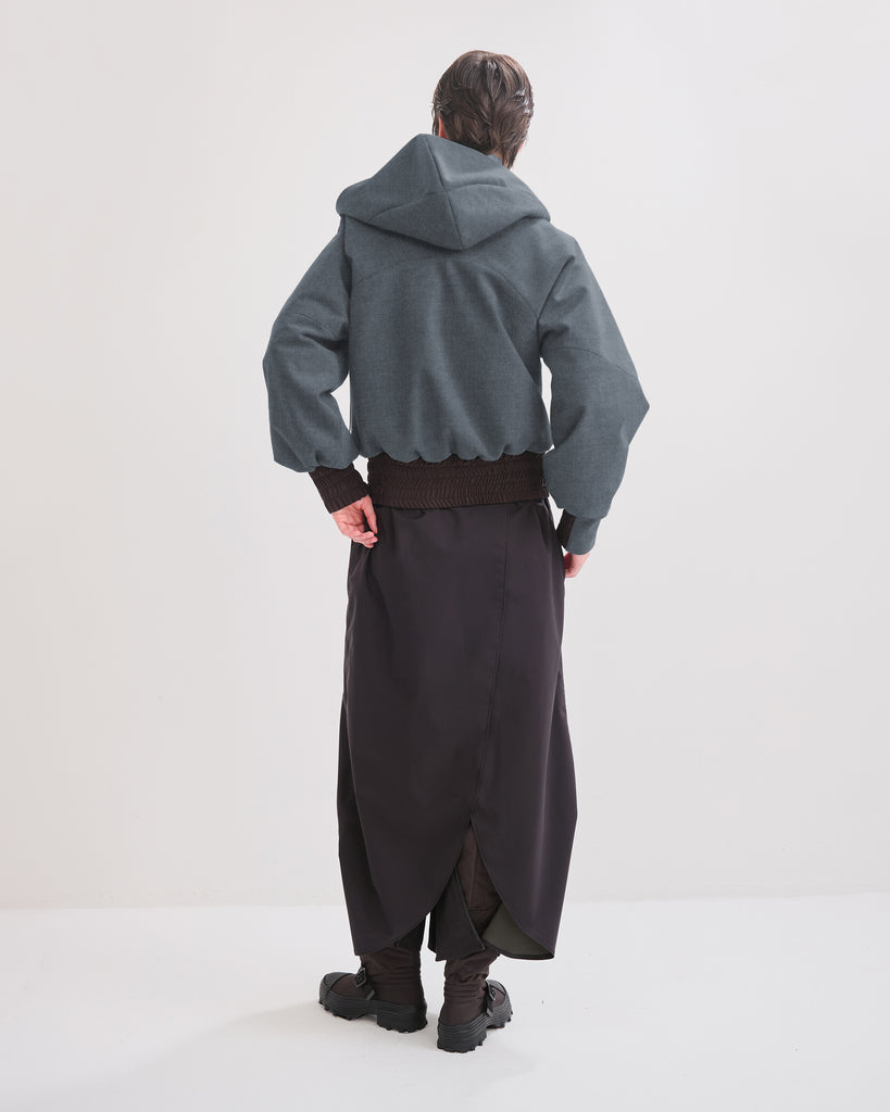 Person wearing a denim hooded jacket and dark rainpants/rainskirt on a white background