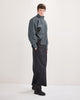 Person wearing a waterproof denim jacket and black rainpants/skirt on a white background